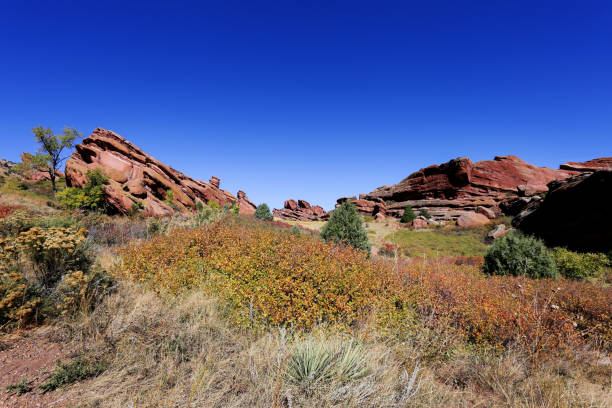 Striking red rock formations rise against a clear blue sky, surrounded by colorful autumn foliage and lush greenery, showcasing the natural beauty of Colorados terrain.