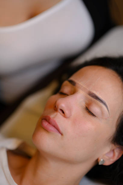 Beautician applying permanent eyebrow makeup on woman