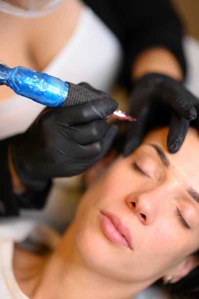 istock Beautician applying permanent eyebrow makeup with microblading machine on brunette hispanic 30 woman 2180372949