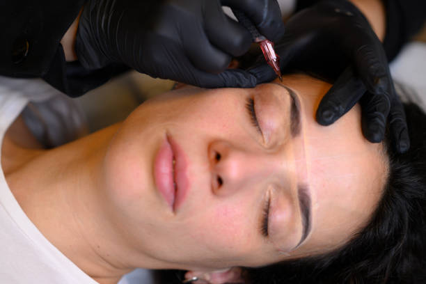 istock Beautician applying permanent eyebrow makeup with microblading machine on brunette hispanic 30 woman 2180372950