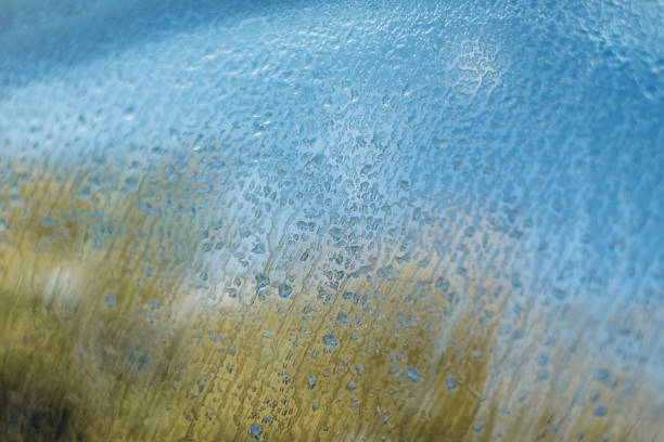 Water droplets on a car windshield reflecting shimmering sunset colors. Selective focus with blurred bokeh lights. Beautiful abstract texture background.