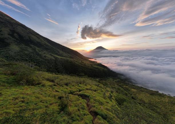 istock Dramatic aerial view of a towering mountain range at dawn. The sun's rays pierce through the clouds, casting long shadows on the rugged peaks. 2180380209