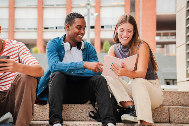 istock Two multiracial teenage studens learning together at university campus. African american schoolboy talking with a school girl about the homeworks. Young friends studying at highschool stairs. 2180382237
