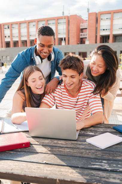 istock Vertical. Group of young classmates studying together and preparing a exam using a laptop, browsing on internet at university campus. Teenage students smiling and doing the homeworks with a computer 2180382525