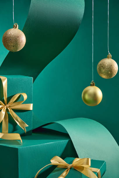 Christmas themed image on luxurious emerald background, features empty product display stands, decorated with green gift boxes wrapped in gold ribbon, Noel balls and green wavy paper.