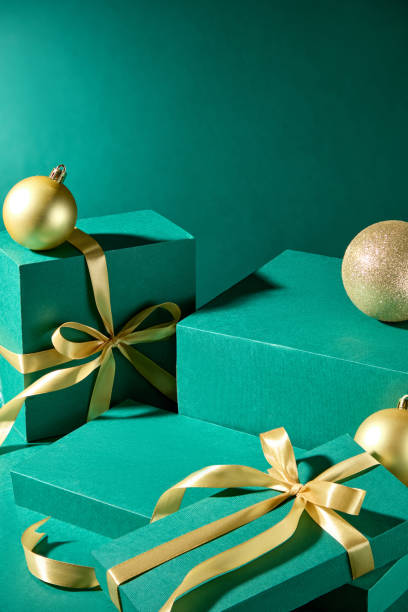 istock A promo image with a Christmas vibe and an emerald backdrop, shows present boxes arranged side by side and an empty rectangular platform for product display, decorated with yellow Christmas balls. 2180388687