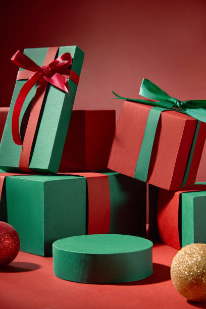 istock The red backdrop creates a Christmas feel for the photo, featuring a round empty platform with product display space placed in the middle, next to gift boxes of various colors with Noel balls. 2180389318