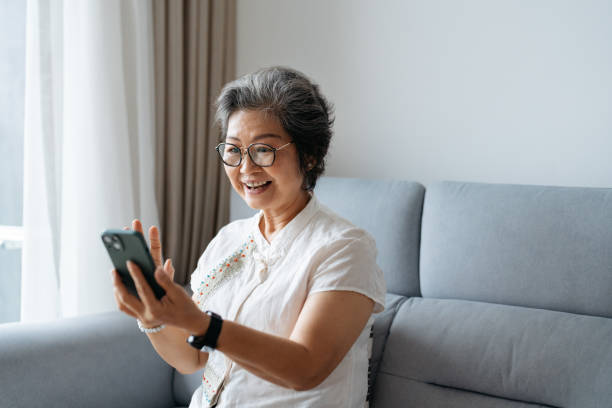 istock Smiling Asian senior woman using smartphone and making a video call 2180389867
