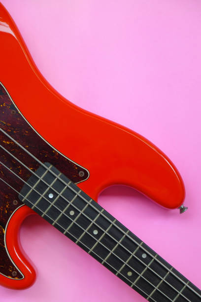 Red electric bass guitar on a pink background. Close-up image.