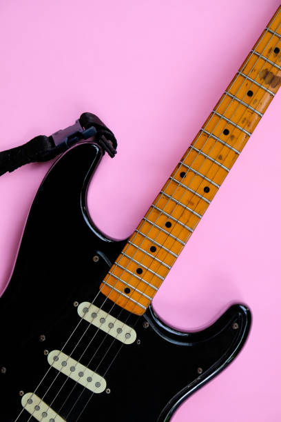 Black electric guitar on pink background. Top view with copy space.