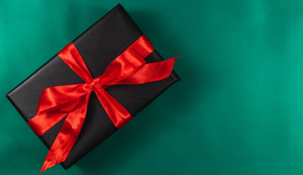 istock Banner with black gift box with red ribbon and bow on green background 2180400252