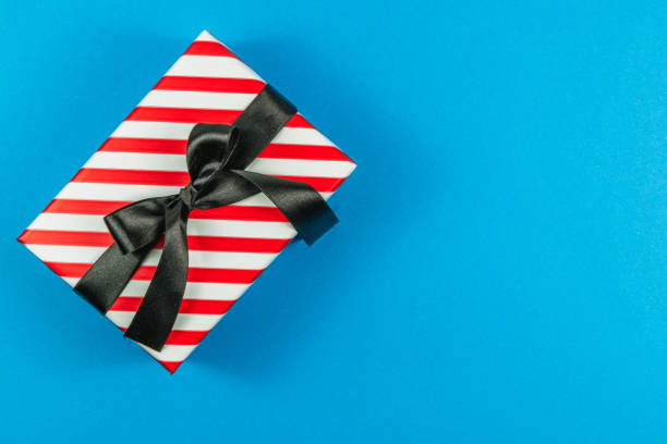 istock A red gift box with white stripes and a black bow on a blue background 2180402161