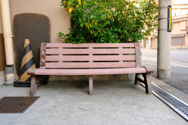 Pink wooden bench and striped traffic cone next to a street.