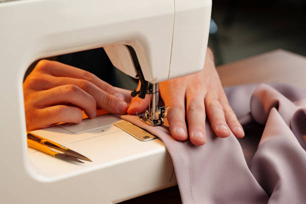 istock Hands sewing fabric using a sewing machine on a wooden table in a well-lit workspace 2180414180