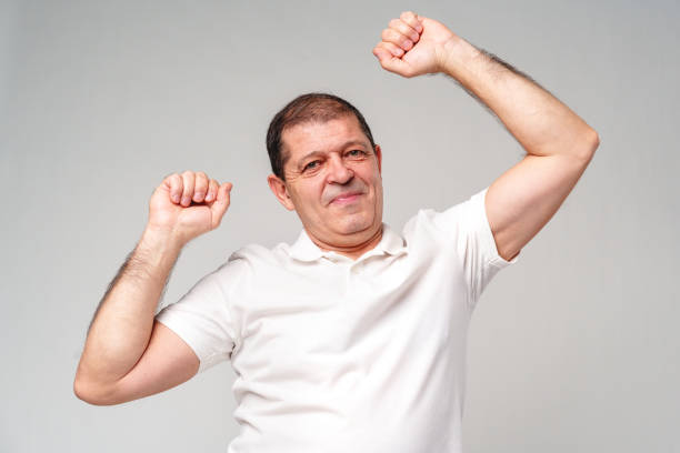 istock Happy older man showing off his strong biceps while standing against a light gray background 2180415412
