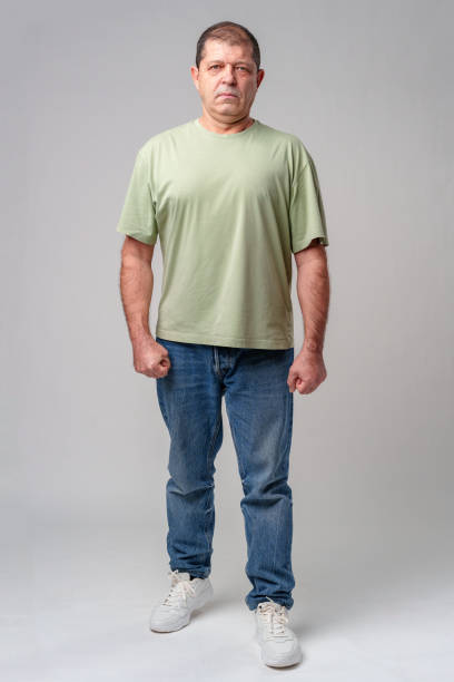Man in casual attire standing posed against a neutral background, displaying a serious expression
