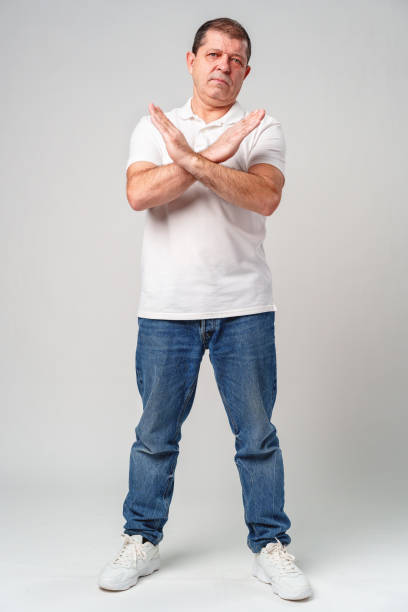 A man making a gesture of refusal with arms crossed against a light background