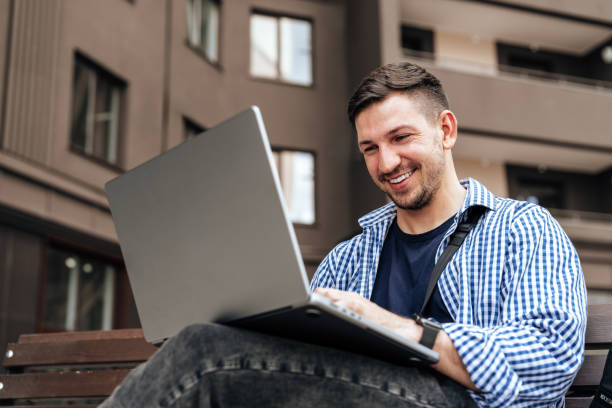 istock Young man working on a laptop while seated on a bench outside 2180417653