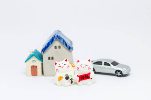 Two lucky cat with miniature house and car model on white background, lucky cat holding sign and gold over miniature house and car on white background