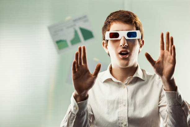 Young businessman wearing a white shirt is using 3d glasses in his office to interact with charts and graphs on a glass wall