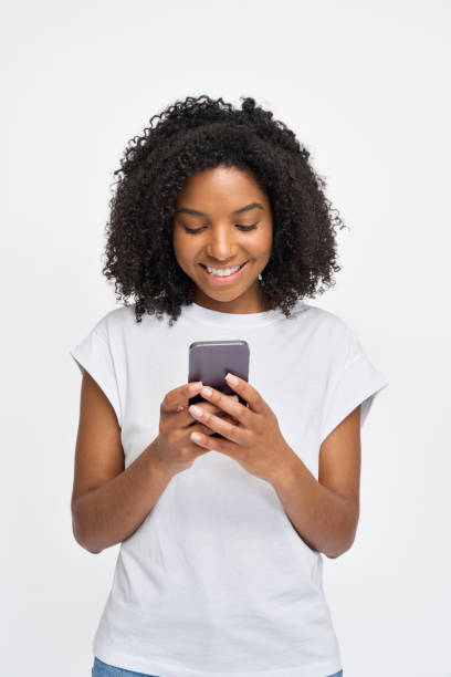istock Young happy African girl standing isolated on white background using smartphone. 2180423073
