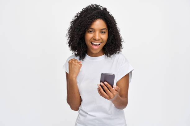 istock Happy African woman celebrating win using phone isolated at white background. 2180423074