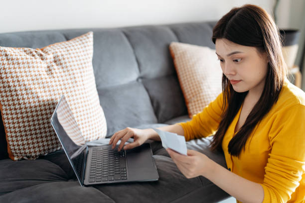 istock Asian woman using laptop and holding receipts while managing finances at home 2180432243