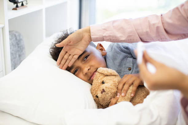istock Young boy in bed with a fever being cared for at home 2180439897