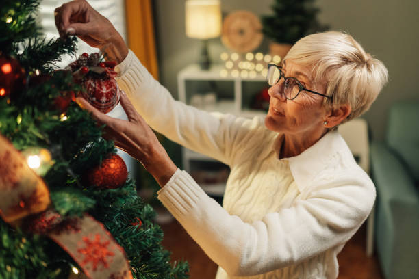 istock Senior woman decorating christmas tree with baubles at home 2180441688