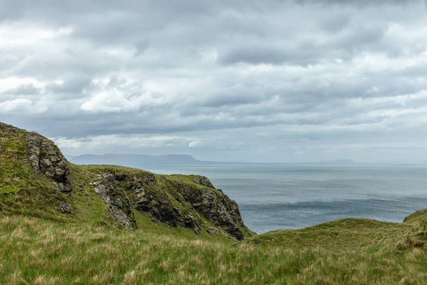 Rugged cliffs along the Irish coastline in County Donegal with green grass and a cloudy sky over the Atlantic Ocean