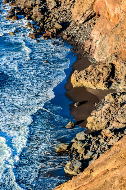 The ocean is calm and the rocks are jagged. The water is blue and the rocks are brown