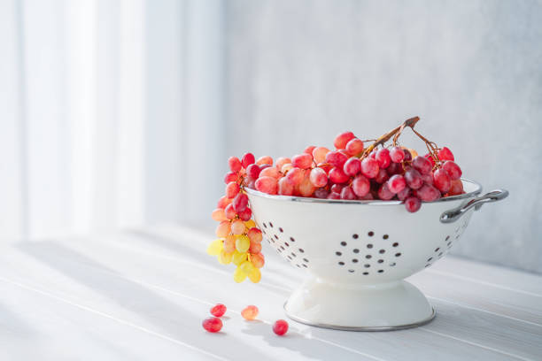 A bunch of pink grapes in a white bowl on a gray background