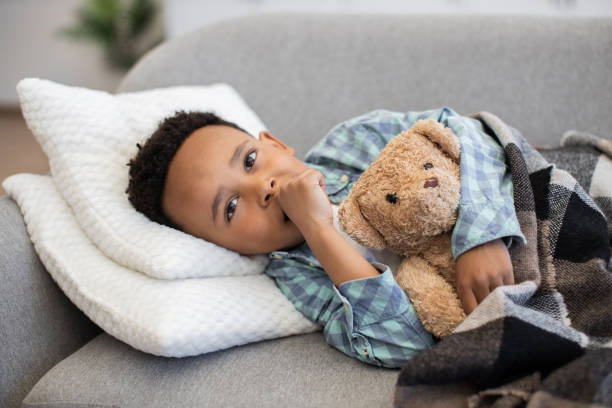 istock Young boy resting on sofa with teddy bear feeling unwell 2180458376