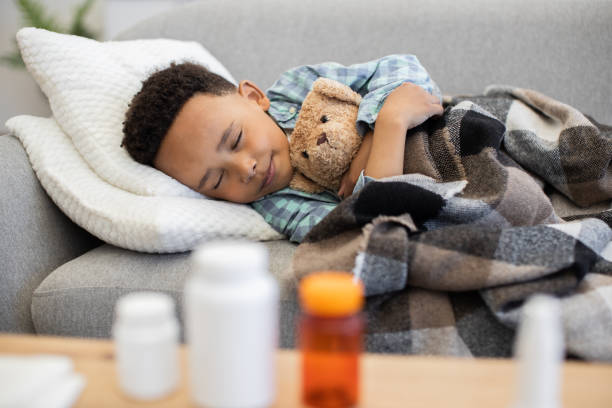 istock Young boy resting on sofa at home with teddy bear and blanket 2180458377