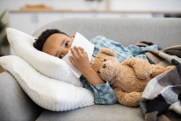 istock Young African boy lying in bed with teddy bear feeling unwell 2180458380
