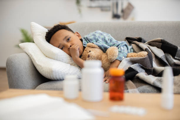 istock Young boy resting with teddy bear during illness on couch 2180458390