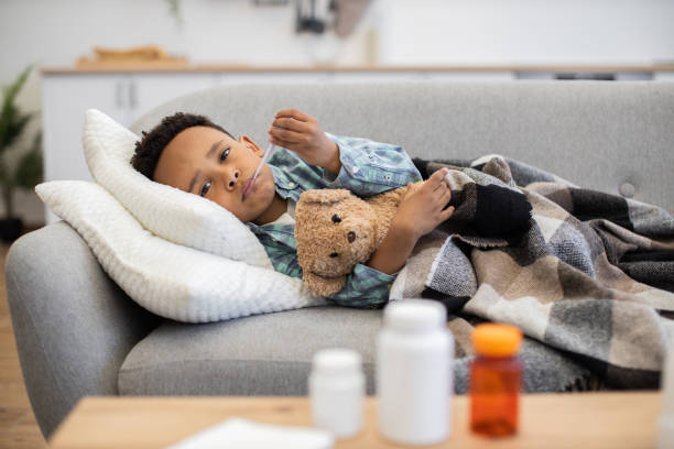 istock Sick boy with thermometer resting on sofa in home kitchen 2180458391