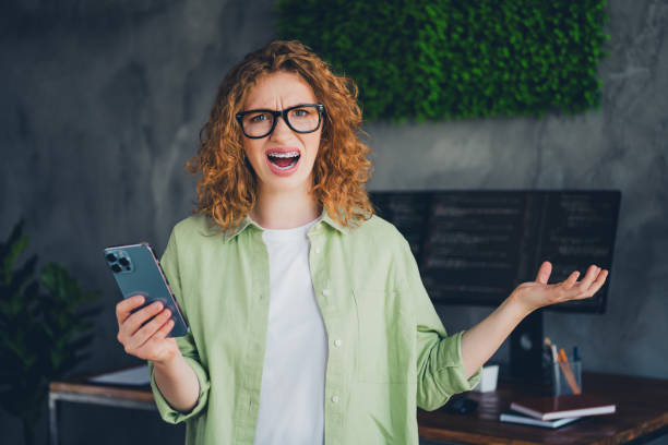 istock Photo of impressed confused lady programmer dressed shirt glasses texting modern device indoors workplace workstation loft 2180458550