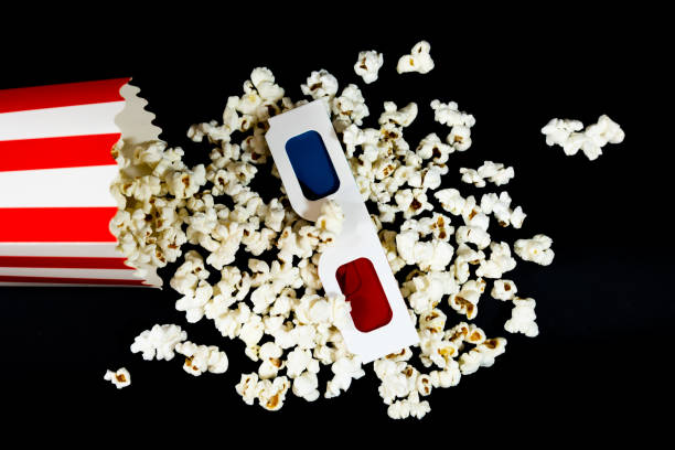 Stock photo showing close-up view of popcorn in two striped cardboard cartons surrounded by spilled popped kernels. Popcorn is a popular snack eaten in movie theatre cinemas.