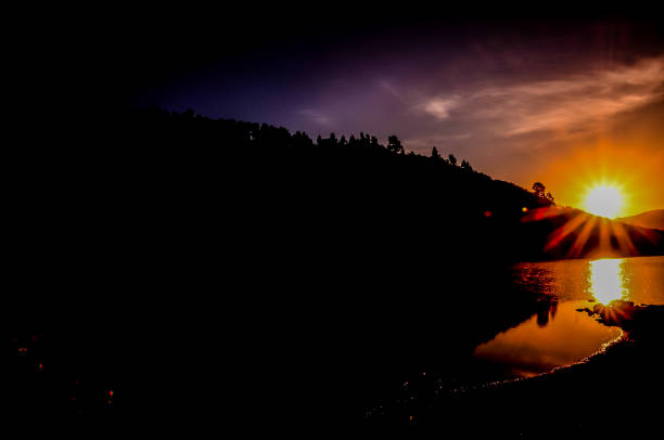A dark sky with a sun in the distance. The sun is shining on the water, creating a beautiful reflection