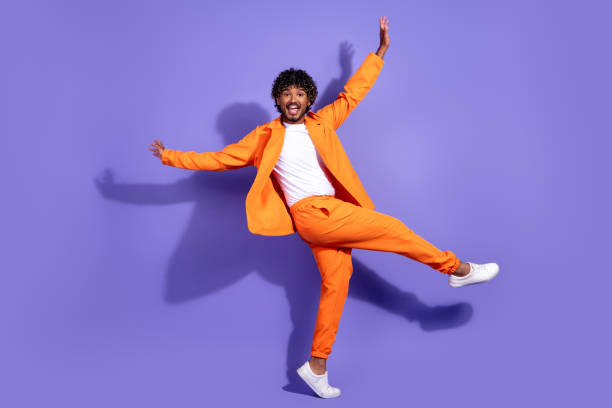 istock Full length photo of funky cool guy dressed orange jacket smiling dancing emtpy space isolated purple color background 2180465247