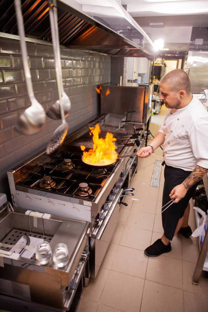 istock Chef cooking with flame in a frying pan on a kitchen stove. 2180467695