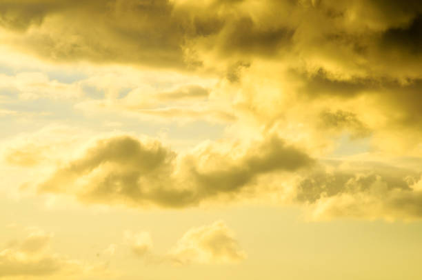 The sky is filled with clouds and the sun is shining through them. The clouds are yellow and the sky is a beautiful shade of orange