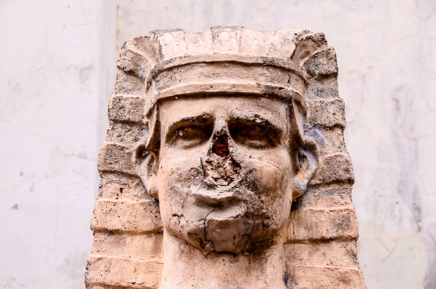 A statue of a man with a missing nose and a scar on his face. The statue is old and has a worn appearance