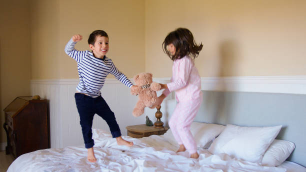 istock Active Children Having Fun Jumping And Playing On Parents Bed At Home With Teddy Bear 2180472075