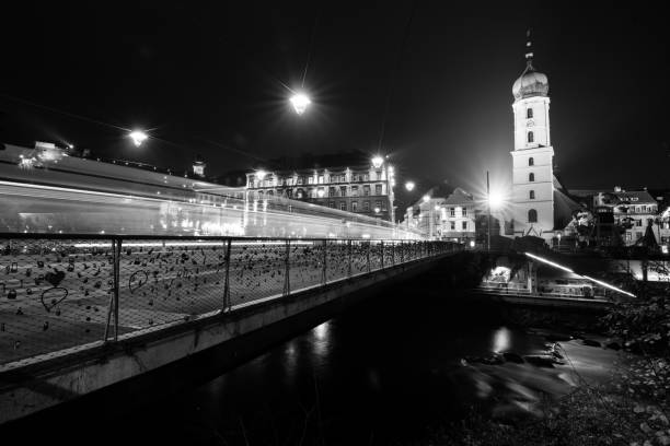 This is a captivating black and white photograph featuring a bridge at night, beautifully illuminated, with a tall tower seen in the background