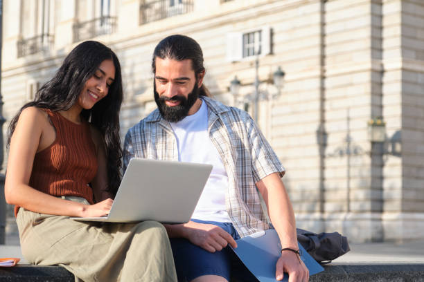 istock Students working on laptop and smiling outdoors in city center 2180476388