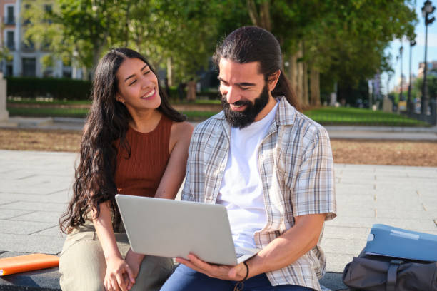 istock Happy couple using laptop and smiling outdoors in a park 2180476780