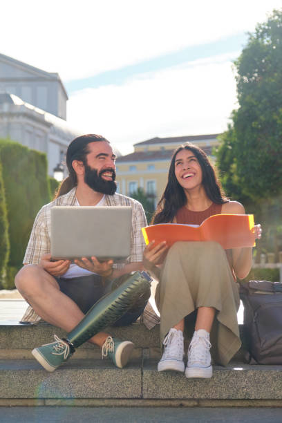 istock Two happy students studying together outdoors with laptop and book 2180477191