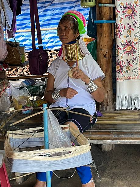 Thailand - Chiang Rai - Karen Village In Chiang Rai province, there is the Karen village which is an indigenous population from Burma. In this photo is represented a woman from the village with a long neck and with gold rings on her neck. She is weaving with her hands and feet, beautiful colored fabrics.08/07/2024